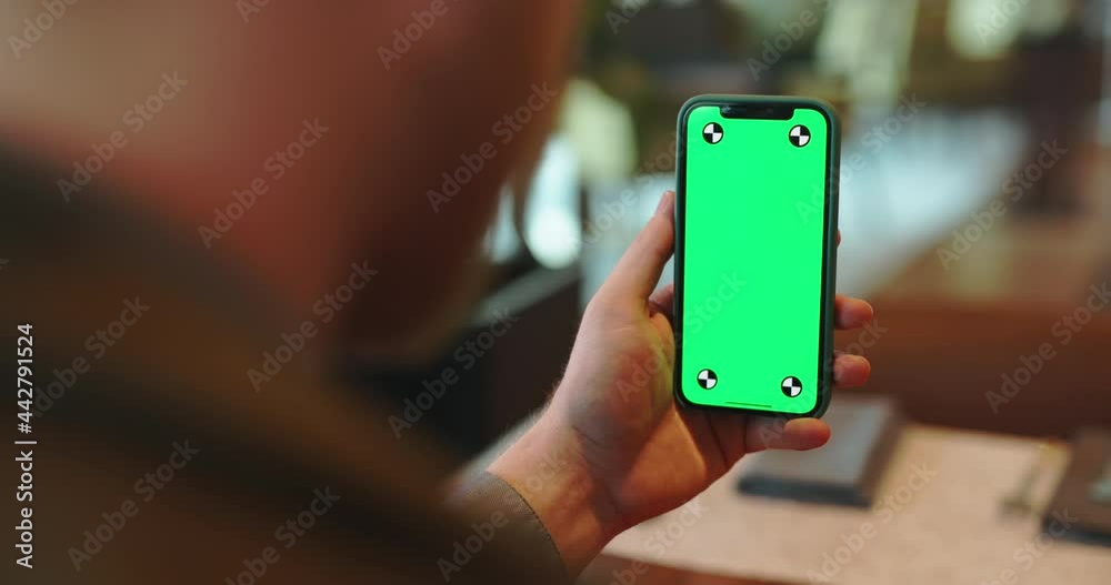 Unrecognizable person using a smartphone with green chroma key display. Man having a video conference in cafe - always online, communication, technology close up 4k footage