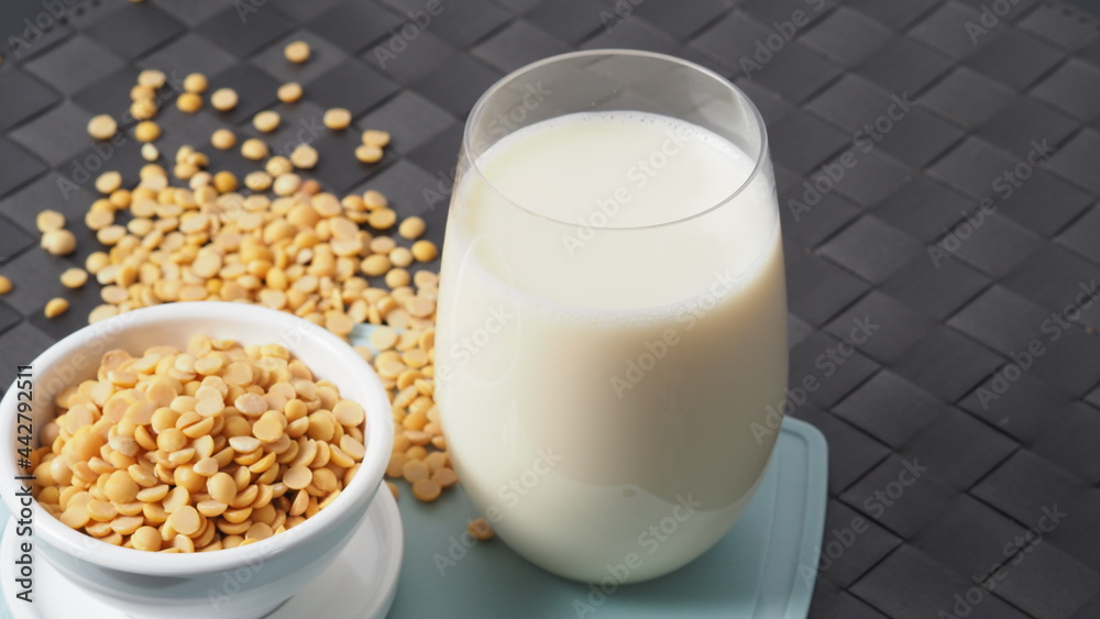 Soy milk with no sugar added in a glass on a green color plastic plate mat. Close-up images of home made healthy soy milk drink and soy beans in small bowl. Black background in a studio shot. Soymilk. Soy milk with no sugar added in a glass on a green color plastic plate mat. Close-up images of home made healthy soy milk drink and soy beans in small bowl. Black background in a studio shot. Soymilk.