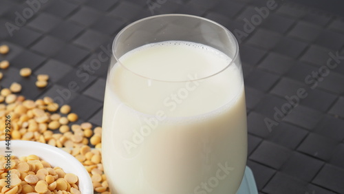 Soy milk with no sugar added in a glass on a green color plastic plate mat. Close-up images of home made healthy soy milk drink and soy beans in small bowl. Black background in a studio shot. Soymilk.