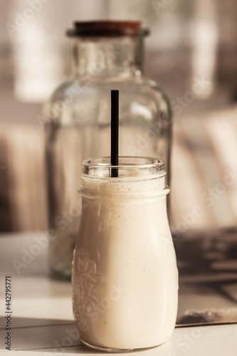 Milk shake  smoothie  in the glass mud with a straw and a glass bottle on wooden table in the beige background. Tasty refreshment in a restaurant or cafe