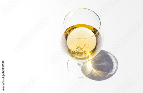 Top view of glass with white fresh wine on white background with sparkling shadows. Free copy space.  Concept of summer drinks.