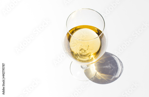 Top view of glass with white fresh wine on white background with sparkling shadows. Free copy space.  Concept of summer drinks.