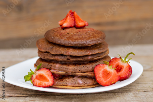 chocolate pancakes with strawberries on a white plate.