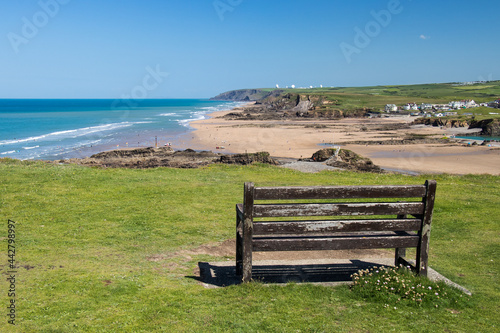 Wooden bench on Cornish cliff overlooking crooklets beach in Bude, Cornwall on a sunny day with a blue sky.