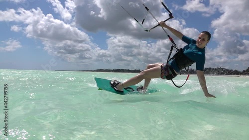 SLOW MOTION, CLOSE UP: Happy young woman kiteboarding in Tanzania drags her hand along the surface of crystal clear ocean. Fit female kiteboarder surfs around the blue lagoon in stunning Zanzibar. photo