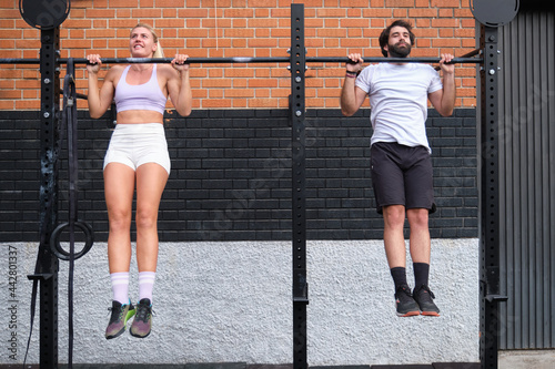 Young man and woman doing pull ups at a crossfit pull up bar