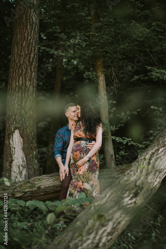 Pregnancy  parenthood concept. Happy pregnant couple  standing in beautiful summer forest  hugging and smiling each other