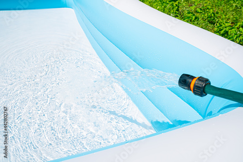 Filling the garden children's pool with water on the green lawn. photo