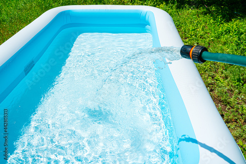 Filling the inflatable pool with water. Swimming pool in the summer garden. photo