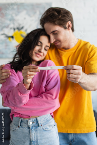 pregnancy test in hands of blurred smiling young couple hugging with closed eyes at home