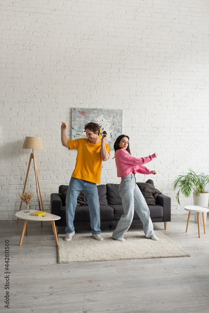 positive young couple in casual clothes dancing in living room