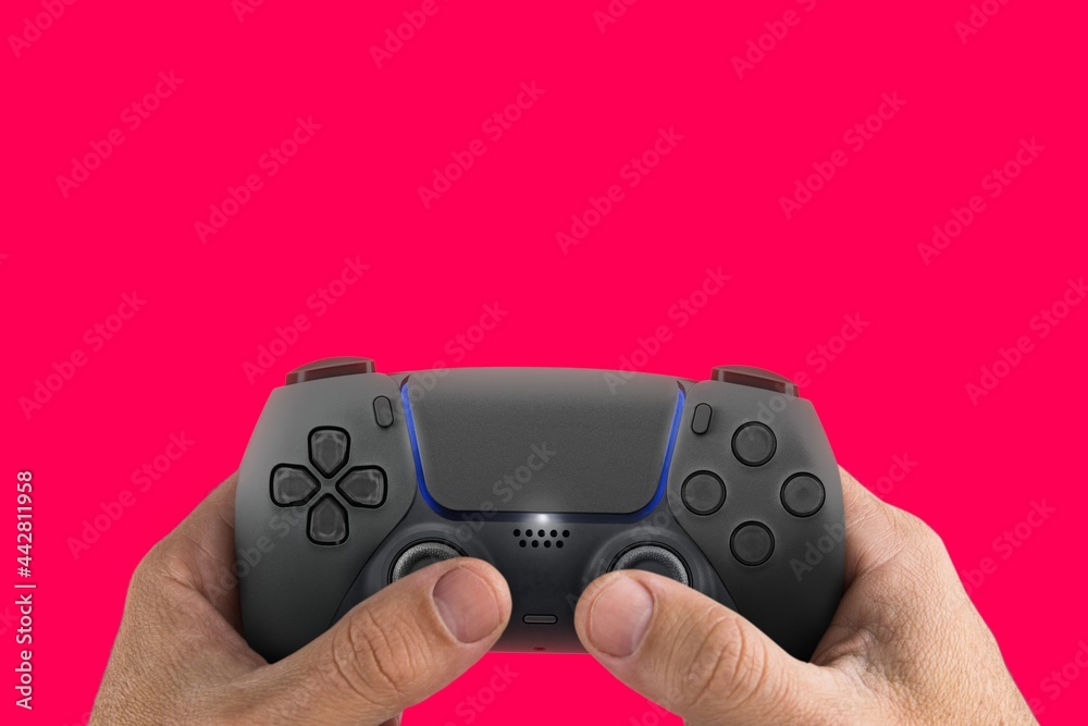 Male hand holding a Next Generation black game controller isolated on pink background. Male hand holding a Next Generation black game controller isolated on pink background.
