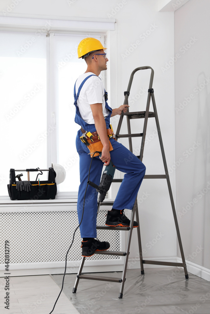 Worker with electric drill on ladder indoors Worker with electric drill on ladder indoors