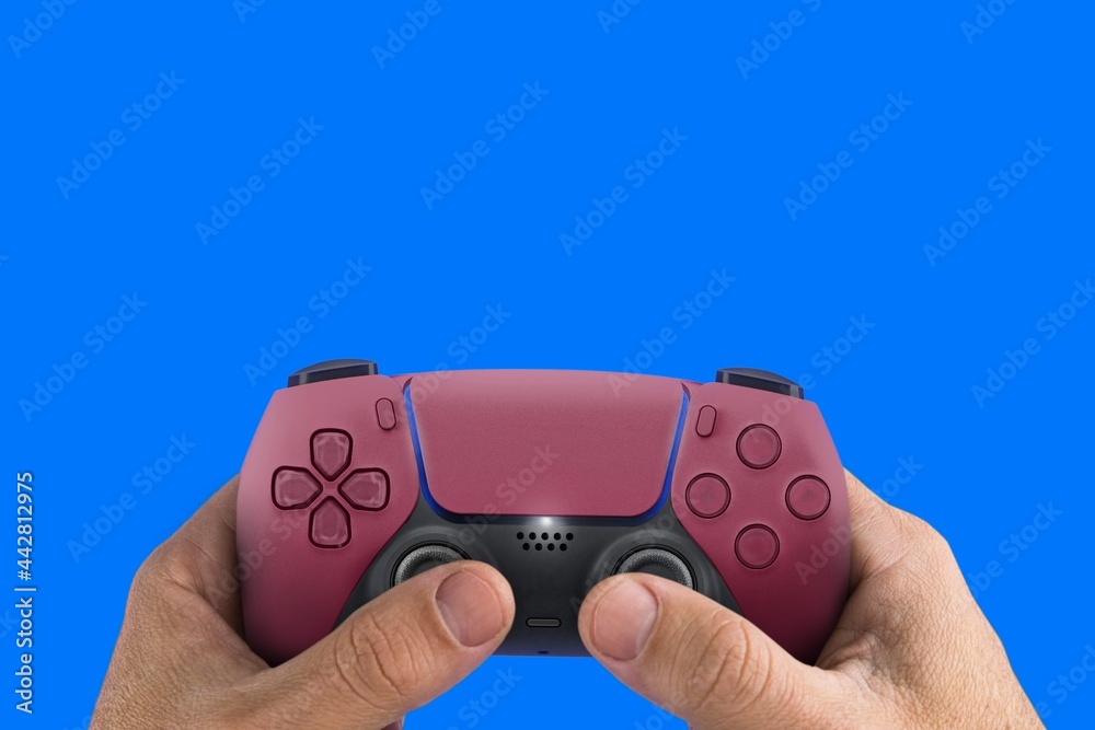 Fototapeta premium Male hand holding a Next Generation red game controller isolated on blue background.