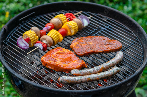 Colorful vegetable skewers, steaks and sausages on a charcoal grill during a barbecue party.