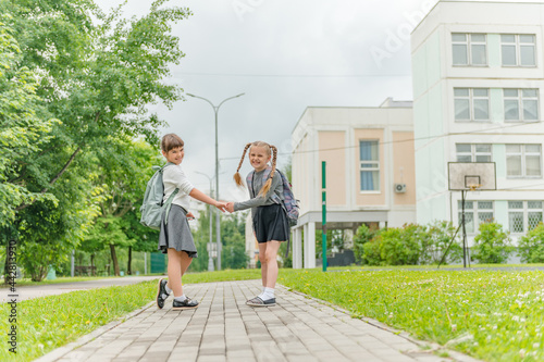 two cute happy girls schoolgirls with backpacks are playing near the school. High quality photo