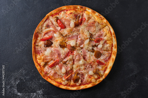 Pizza with tomatoes, bacon, pickled onions, honey mushrooms, mozzarella cheese, spices and tomato sauce. Flat lay. On a dark background.