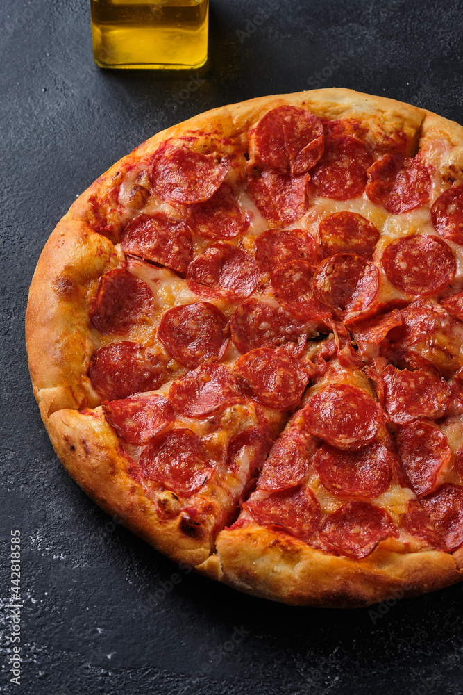 A closeup of a pepperoni pizza. Pizza with spicy sausage, tomato sauce and mozzarella cheese. Flat lay. On a dark background. A closeup of a pepperoni pizza. Pizza with spicy sausage, tomato sauce and mozzarella cheese. Flat lay. On a dark background.