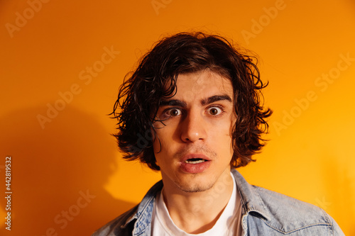Amazed man in denim shirt looking at camera on orange background