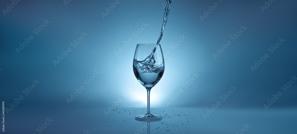 banner with pouring water into a transparent glass for wine. light blue background with water splashes and copy space banner with pouring water into a transparent glass for wine. light blue background with water splashes and copy space
