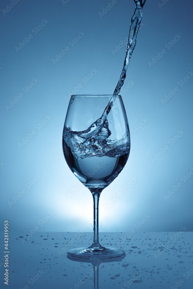 pouring water into a transparent glass for wine. light blue background with water splashes pouring water into a transparent glass for wine. light blue background with water splashes