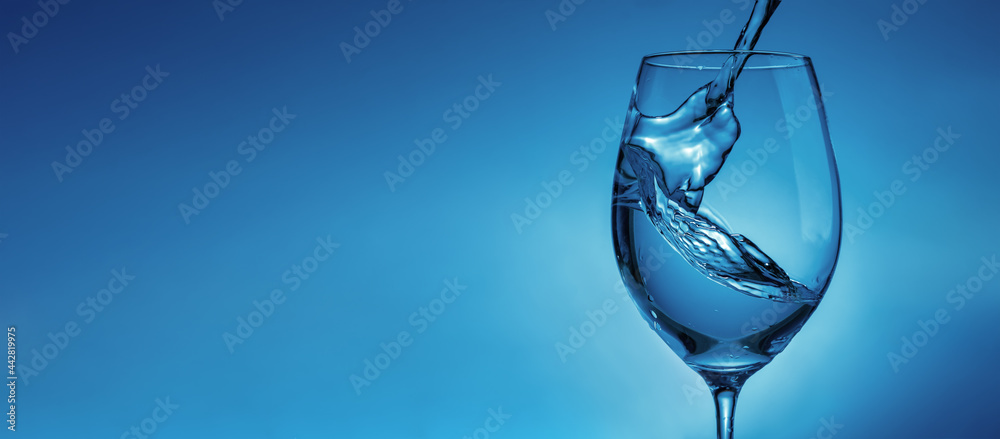 banner with pouring water into a transparent glass for wine close-up. light blue background with water splashes and copy space