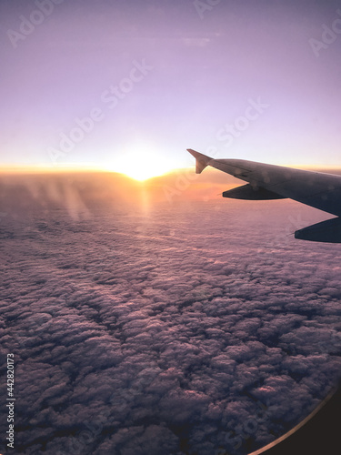 Plane wing flying over the clouds and colorful sunset in the horizon