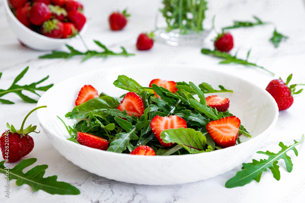 Summer salad of strawberry with arugula, spinach leaves in white plate on marble table with salad leaves and fresh strawberry fruits around. Strawberry salad recipe DIY. Step 2.