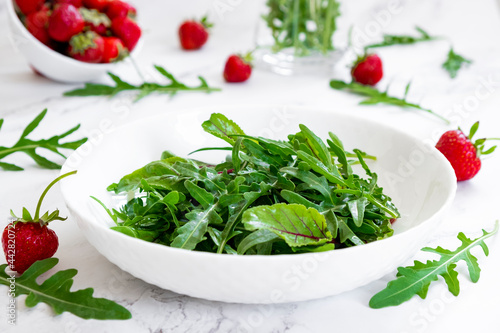 Summer salad of strawberry with arugula, spinach leaves in white plate on marble table with salad leaves and fresh strawberry fruits around. Strawberry salad recipe DIY. Step 1.