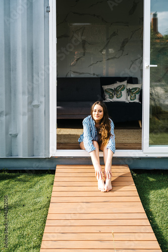 carefree beautiful female sitting in front of modern tiny house