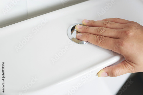 A man's hand pressing a button in the toilet