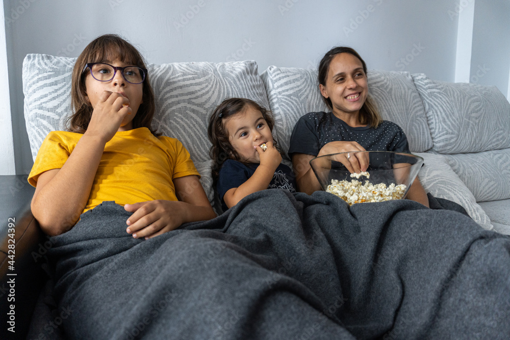 Mother and daughters watching a movie at home and eating popcorn.