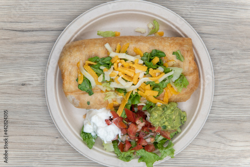Overhead view of enormous chimichanga burrito topped with cheese and served with a scoop of sour cream, guacamole, and pico de gallo for lunch