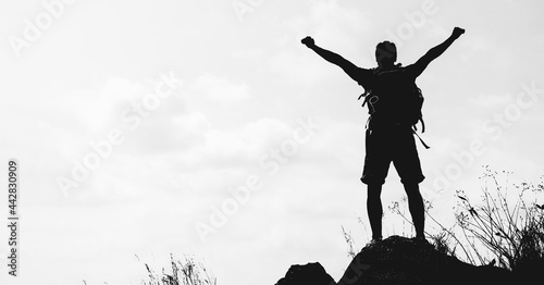 silhouette hiker hiking success on rocky hill top in black and white