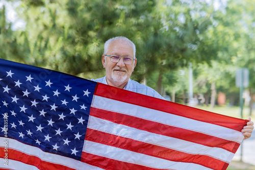 A happy senior patriot wearing a stars and stripes a large American flag. photo