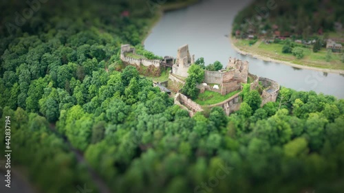 An aerial view of a medieval castle Cornstein located on the top of a green peninsula. Lush trees are densely growing on the hill. A road is running along the peninsula. A tilt shift video. photo