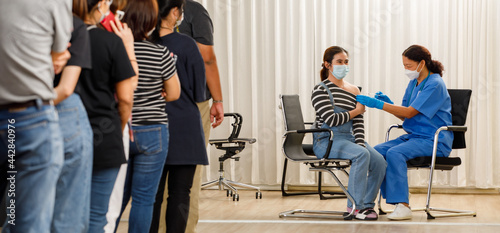Citizens of different ages in a row standing and waiting for a vaccine injection while medical people injecting to young woman in face mask. Covid-19 or coronavirus vaccination service concept photo