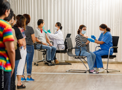 Variety ages citizens standing in a row and waiting for a vaccine injection while medical people injecting to young woman and old man in face mask. Covid-19 herd immunity concept