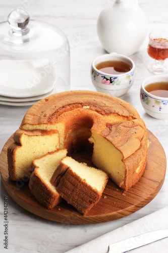 Slice of Fluffly Vanilla Chiffon Cake or Sponge Cake on Wooden Plate, Served with Tea and Honey. Bright Food Photography Concept for Bakery. Selected Focus