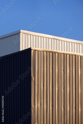 Perspective side view of gray and white corrugated metal wall of  industrial buildings against blue sky in vertical frame