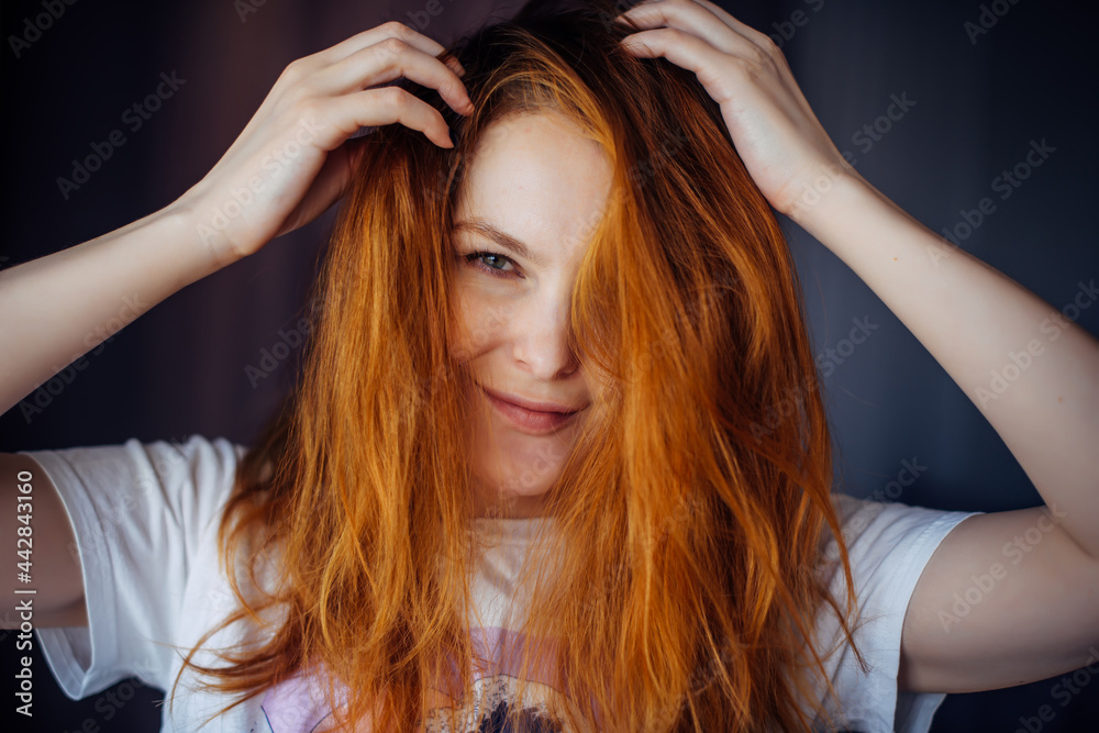 Fototapeta premium Portrait of beautiful adult young woman with red tousled hair, close-up, blurred background. Sexy brunette touches her long hair and looks at camera.