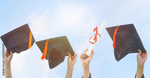 The hand is holding the graduation hat and certificate with a beautiful blue sky background