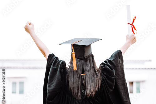 Woman in gowns raise their hands show signs of happiness after graduation with a graduation certificate.