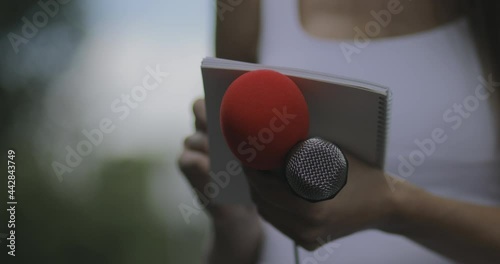 Female journalist at news event writing notes, holding microphone photo
