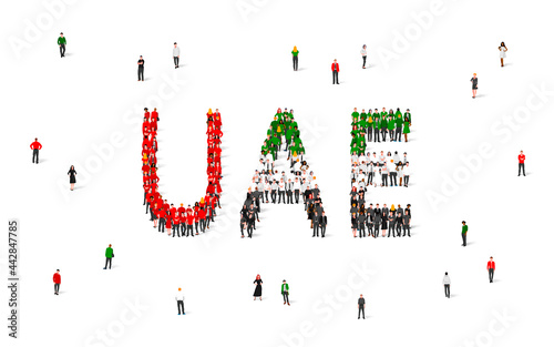 A crowd of people stands in red, green, white and black clothes, making up the word UAE. UAE flag made from people.