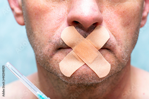 the concept of universal vaccination and freedom of speech a person's mouth is sealed with a medical plaster next to a syringe for injection