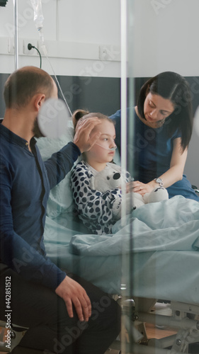 Sick daughter wearing oxygen nasal tube lying in bed after illness surgery waiting for medical examination with parents in hospital ward. Hospitalized child recovering after flu isickness nfection photo