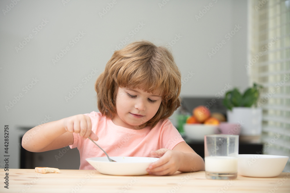 Caucasian toddler child boy eating healthy soup in the kitchen. Closeup face of cute little boy eating tasty porridge or cereals with milk at home, sitting at table in kitchen. Caucasian toddler child boy eating healthy soup in the kitchen. Closeup face of cute little boy eating tasty porridge or cereals with milk at home, sitting at table in kitchen.