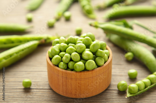 Green peas in wooden bowl on grey background.