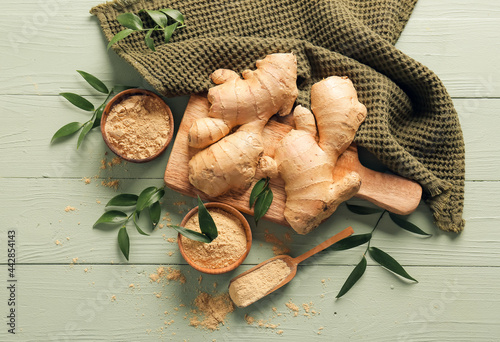 Bowls with ground ginger and roots on color wooden table photo